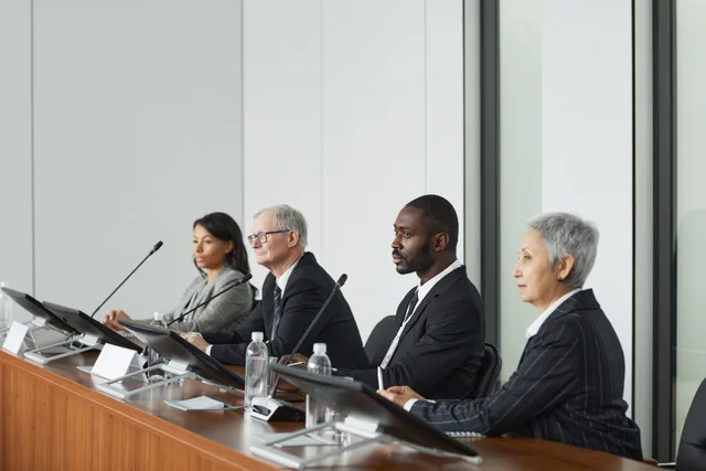 Professional business panel meeting in a modern office setting with four diverse executives seated at a table. Commerce reviews: five hidden cost lines