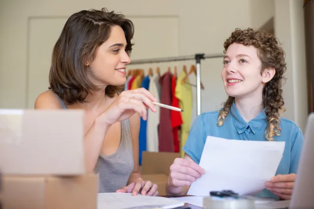 Two businesswomen discussing ideas in an office setting with clothing in the background. Commerce reviews: five launch artefacts for ecommerce teams
