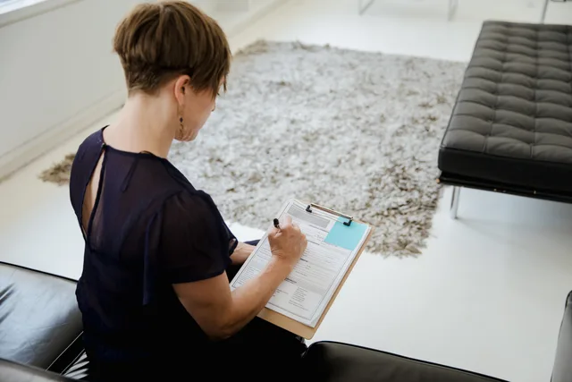 A woman sitting indoors writing on a clipboard, focused on completing paperwork. Seven steps to a commerce reviews operating workflow