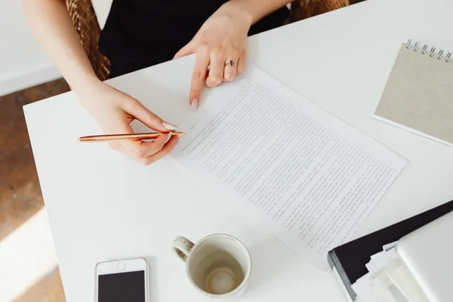 Close-up of a woman reviewing a document at a white desk with a pen. When to put commerce reviews service standards in writing